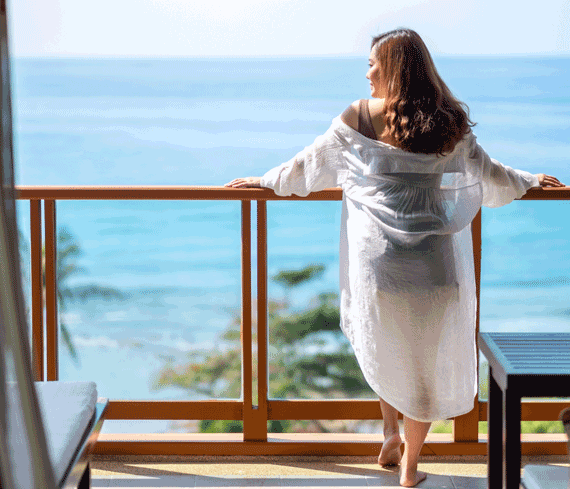 Woman on vacation leaning over railing with beach view